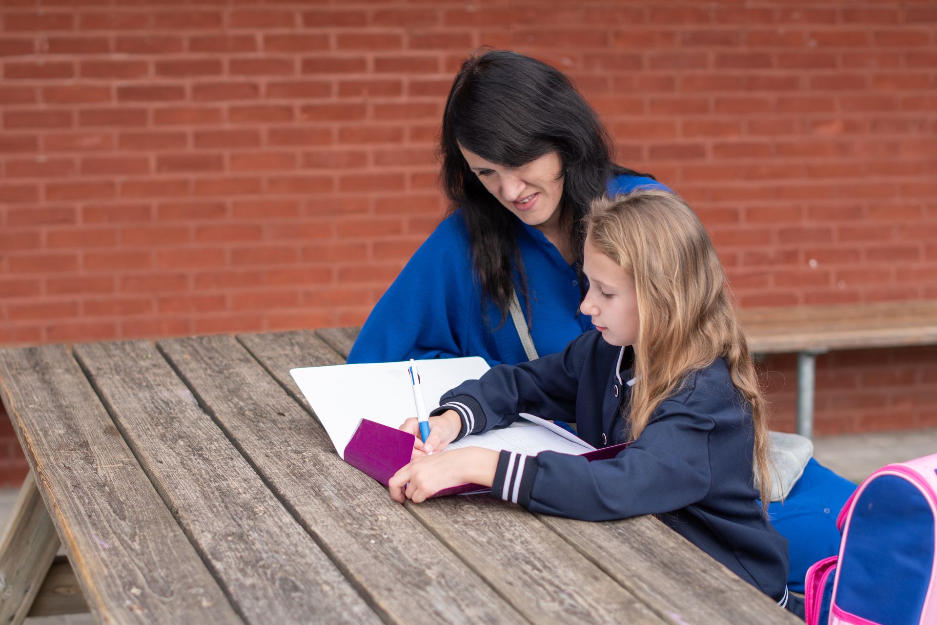 Mutter und Tochter besprechen Hausaufgaben im Freien an Holzbank