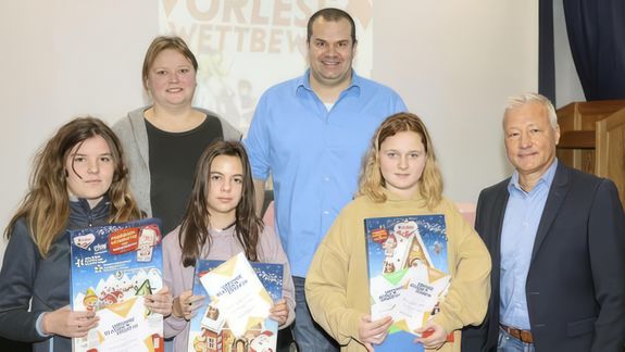 Das Foto zeigt (vorne, v. li.) die Klassensiegerinnen Veronika Sattler (6a) und Lena Reusch (6b) sowie Schulsiegerin Laura Momberg (6c) mit Schulleiter Klaus Förster (re.), Lehrerin Corinna Vogl und Moderator Andreas Rauch.