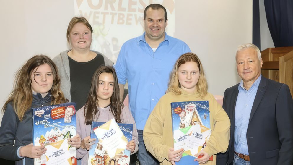 Das Foto zeigt (vorne, v. li.) die Klassensiegerinnen Veronika Sattler (6a) und Lena Reusch (6b) sowie Schulsiegerin Laura Momberg (6c) mit Schulleiter Klaus Förster (re.), Lehrerin Corinna Vogl und Moderator Andreas Rauch.